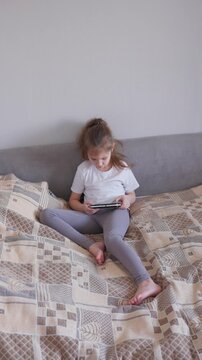 Young Caucasian Girl Relaxing With Handheld Device. Young Woman Of Caucasian Descent Playing Video Game During Leisure. Casual Scene Featuring Young Caucasian Female Engaged In Gaming On Sofa At Home