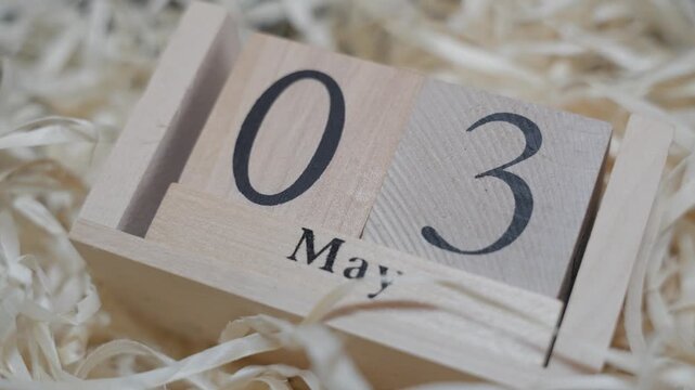 Angled view of wooden desk calendar set to May 3. Perspective shot adds depth while maintaining focus on simple numeric layout.