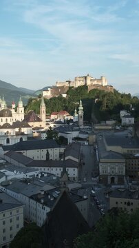 Vertical video of the historic streets of Salzburg, Austria, leading up to the medieval Hohensalzburg Fortress on the hill during the daytime.