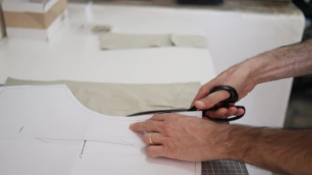 Tailor precisely cutting fabric with scissors along paper pattern while preparing garment design in workshop