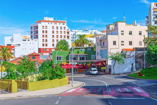 Icod de los Vinos in Tenerife residential street with colorful buildings, curved road descending through hillside town. Lively Canary Islands urban scene with cafes and traditional architecture