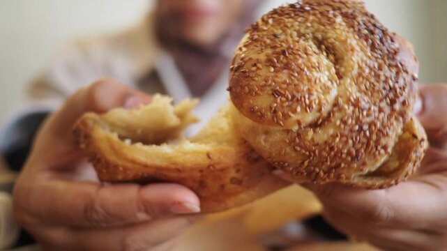 Close up hands breaking tasty bagel with sesame seeds, person enjoying fresh pastry, morning snack.