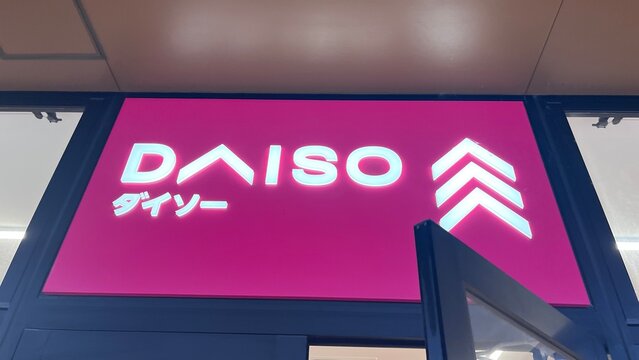 Daiso discount store illuminated storefront sign with signature pink background and white logo at a commercial shopping center - Tokyo Metropolitan, Japan, April 14, 2024