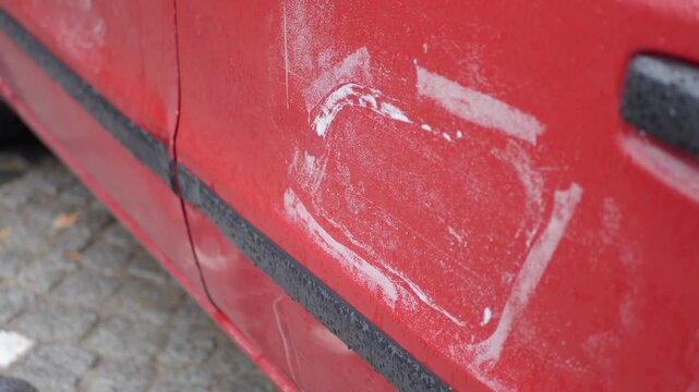 Red car door with white paint patch and water droplets after rain.