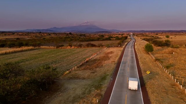 Light traffic on a state highway between Puebla and Cuernavaca (Mexico) with Popocatepetl volcano in the background at sunset. Drone camera flies over the route to the volcano