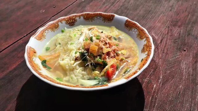 A delicious serving of chicken soto, a traditional Indonesian soup made with flavorful broth, tender chicken, and aromatic spices, presented on a wooden table.
