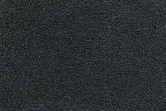 Detailed texture of dark grey sherpa fleece fabric. Top view close-up of soft curly textile material for outerwear and interior design