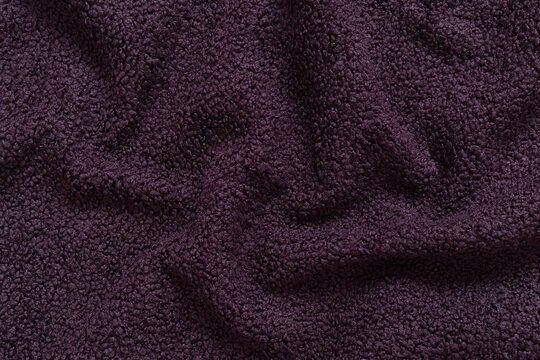 Detailed texture of dark purple sherpa fleece fabric. Top view close-up of soft curly textile material for outerwear and interior design softly draped to create an abstract background