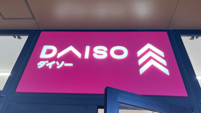 Daiso Industries storefront signage with white illuminated logo and company name in katakana on vibrant pink background above glass entry - Tokyo, Japan, October 15, 2024