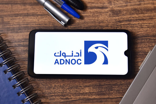 ADNOC (Abu Dhabi National Oil Company) logo on a smartphone screen with office objects in the background. Abu Dhabi's state-owned oil company and one of the world's largest energy producers.