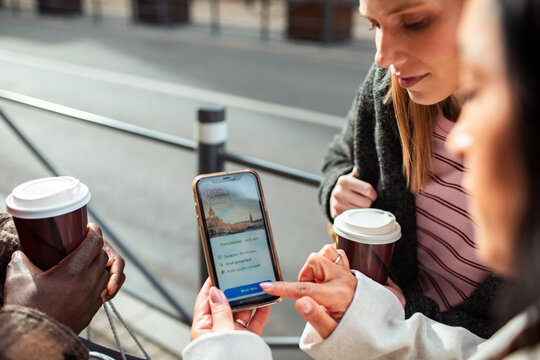 Friends booking a historic walking tour on smartphone in city street