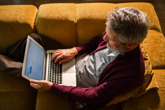 Middle-aged man using laptop on sofa at home