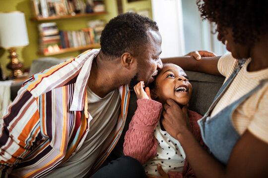 Parents tickling daughter on sofa at home
