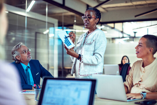 Senior woman presenting sales data to team in modern office