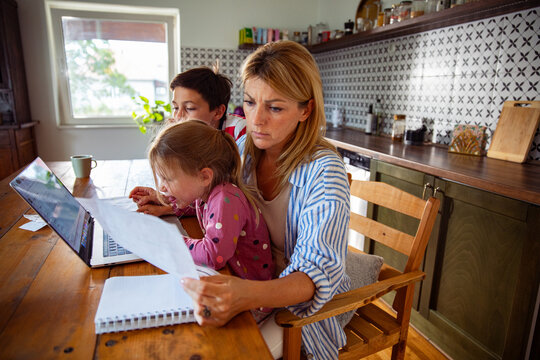Stressed mother managing bills with children at kitchen table