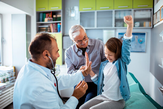 Pediatrician high-fives child patient with caregiver in clinic