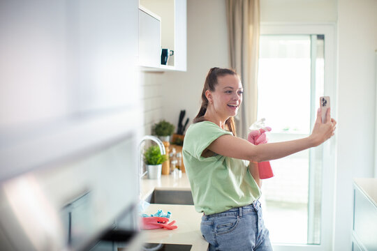 Young woman taking selfie while cleaning kitchen