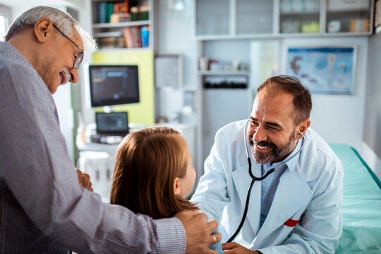 Pediatrician greeting child with parent in clinic exam room