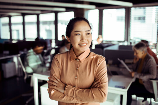 Confident businesswoman with arms crossed in modern open-plan office