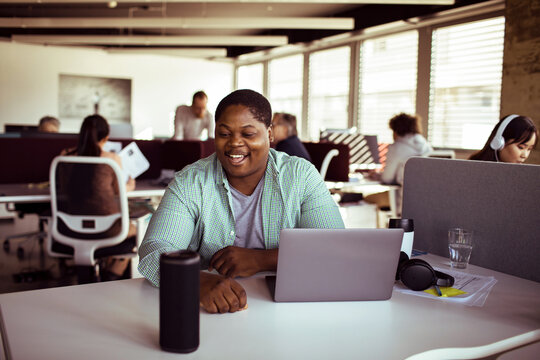 Smiling office worker using smart speaker in open plan coworking space