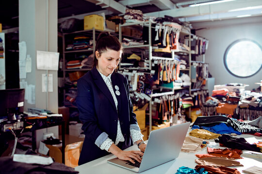 Female fashion designer using laptop in fabric studio