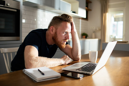 Worried man working on laptop in home kitchen