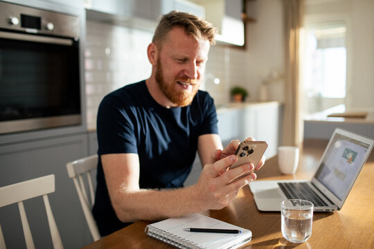 Smiling man using smartphone while working from home kitchen