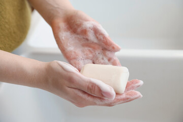 Fototapeta premium Woman washing hands with soap bar against blurred background, closeup