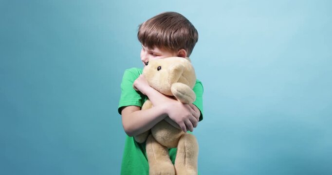 Little boy hugging his teddy bear on light blue background