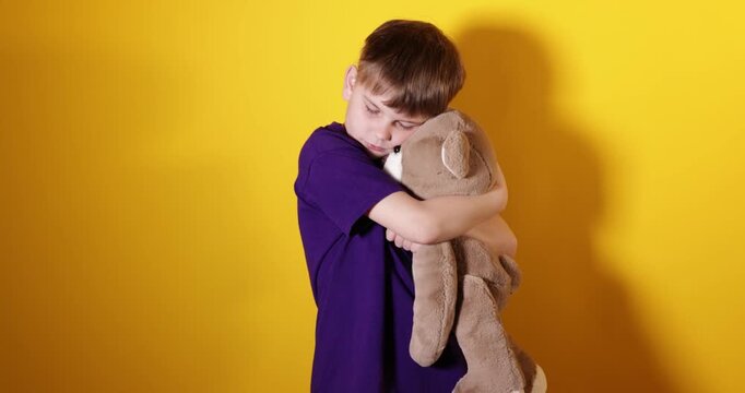Upset little boy hugging his teddy bear on yellow background