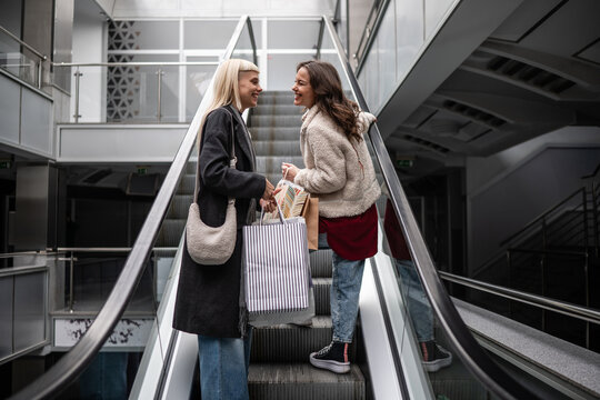 Happy young women friends shopping on escalator