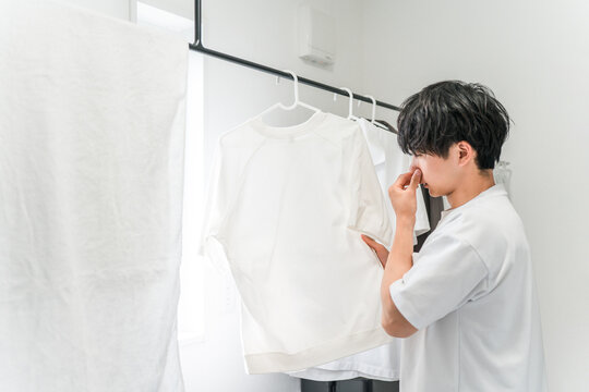 A young man is troubled by the smell of his laundry and the musty smell of damp clothes (damp clothes, drying indoors, smell, laundry room).