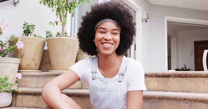 Woman reacting to off-camera voice, shifting on front steps and turning laughter toward camera