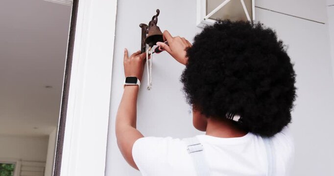 African American woman tightening loose bell with screwdriver at front entry, ensuring cord hanging
