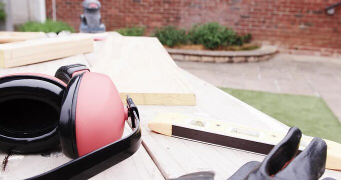 Camera pulling back, revealing earmuffs, spirit level, gloves and planks on bench showing workspace