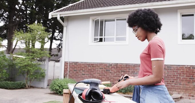 African American woman surveying bench at home picking gloves  and  checking tool by sander, copy sp