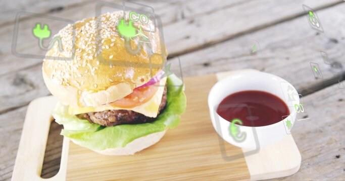 Displaying sesame burger resting on wood board with cheese, ketchup bowl and AR icons, copy space
