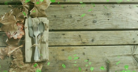 Breeze lifting leaves and sending green specks as tied cutlery resting on linen napkin evoking fall © vectorfusionart