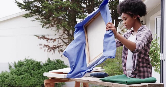 African American woman inspecting stretching blue fabric over frame on porch bench, copy space