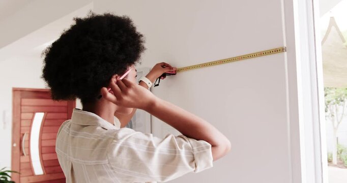 African American woman measuring wall by door for hanging, checking tape and making pencil mark