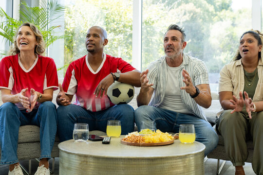 Late goal chance sparking group of four fans reacting on sofa, holding soccer ball, watching match