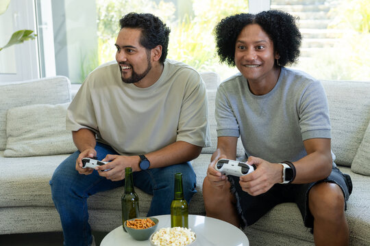 African American male friends sitting on light sofa playing games with white controllers and beer