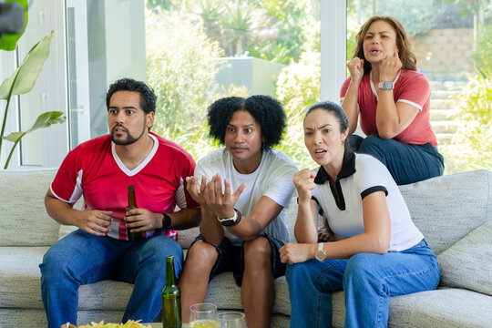 African American friends watching game, reacting on light sofa in living room with beer, chips