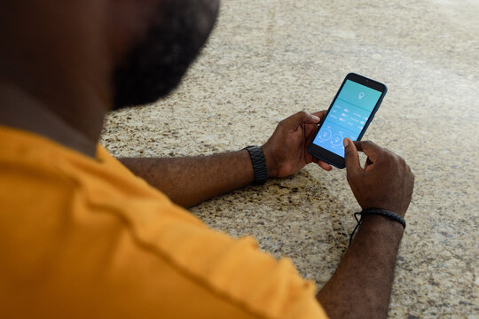 Mid-adult African man tapping smartphone on kitchen counter in orange, watch, bracelet, copy space