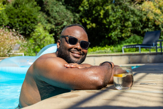 Mid-adult African American man leaning on pool coping, smiling, sunglasses, wristband, lemon glass