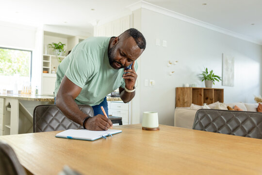 Smartphone sitting on open notebook with pencil and ceramic mug on wooden dining table near window