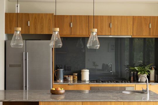 Kitchen island and stone countertop showcasing wooden fruit bowl, sink, pendant lights in kitchen