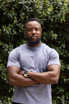 African man standing arms crossed in garden wearing athletic tee, smartwatch and small studs