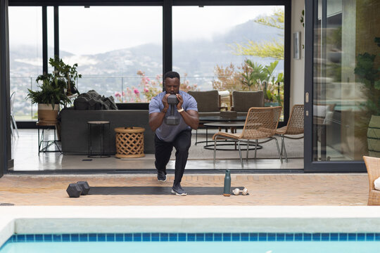 Adult man performing weighted lunge at pool patio wearing athletic clothes and holding kettlebell