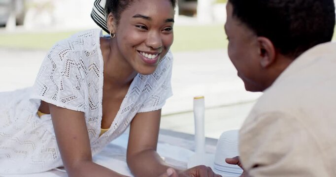 Couple touching hands on picnic blanket laughing and connecting near sunhat and white bottle